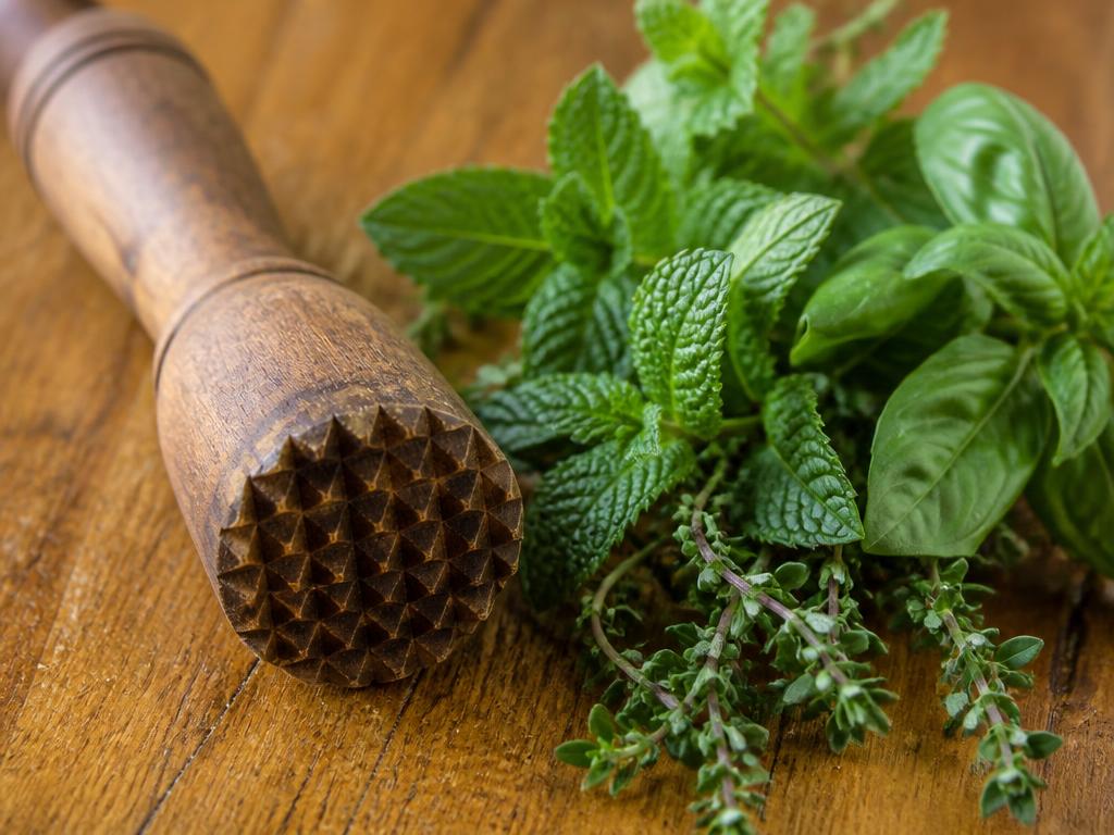 A wooden muddler beside fresh herbs on a wooden board