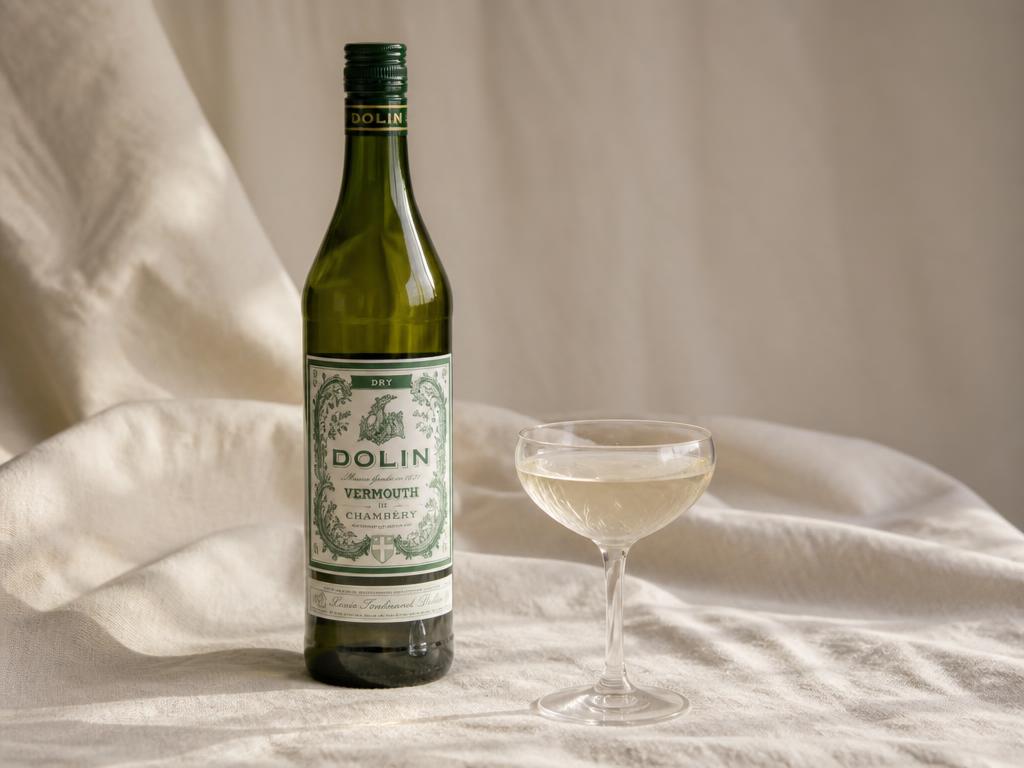 A bottle of dry vermouth and a coupe glass on cream linen